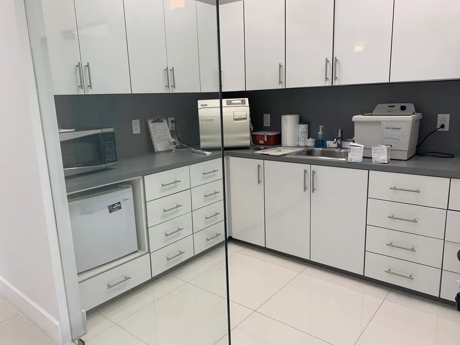 Un &aacute;rea de esterilizaci&oacute;n de la cl&iacute;nica con un autoclave de vapor sobre un mostrador limpio y gabinetes blancos